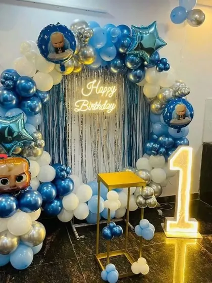 A Boss Baby first birthday setup with a blue and silver balloon arch, a "1" marquee number, and a shimmering curtain backdrop.