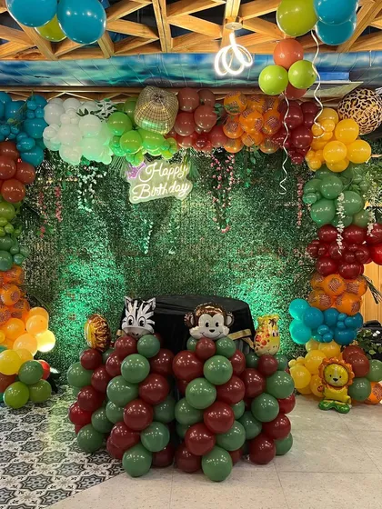 The full view of the jungle party backdrop, with a 'Happy Birthday' neon sign and a colorful balloon arch.