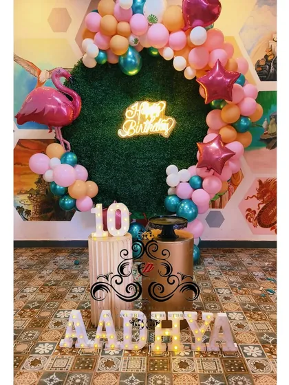For birthdays, I bring any theme to life. This tropical jungle theme for a 10th birthday includes a custom grass backdrop, a neon 'Happy Birthday' sign, themed balloon arrangements, and light-up marquee numbers.