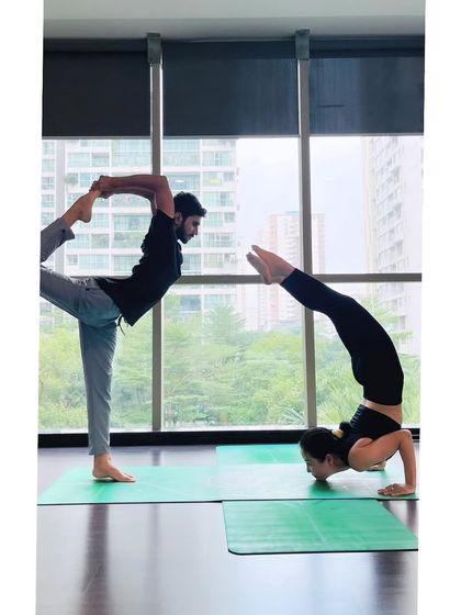 A partner yoga pose combining Natarajasana (Dancer's Pose) and a chin stand, creating a beautiful shape of balance and trust.