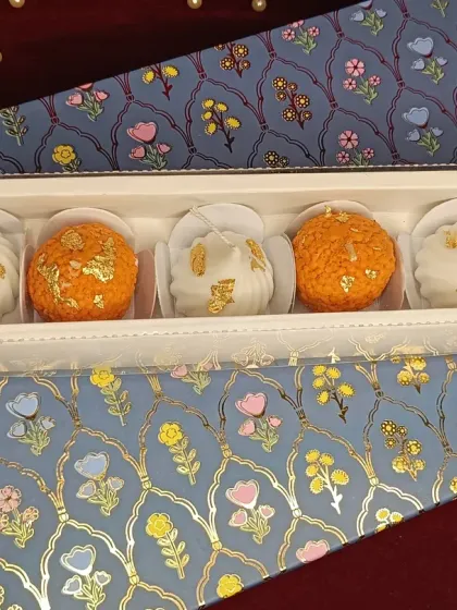 The 2-laddoo and 3-modak candle set, presented on a decorative floral paper, ready for gifting.