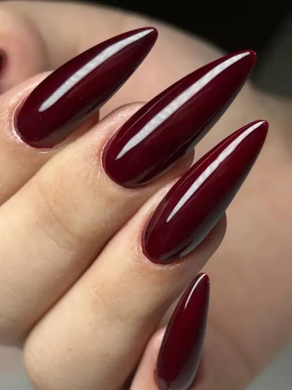 A deep, glossy burgundy on long, stiletto nails. The sharp shape and dark color create a dramatic and high-fashion look.