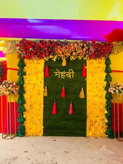 This Mehndi backdrop combines a green turf panel with yellow drapes and colorful tassels. The mix of textures and colors creates a rich and festive look.