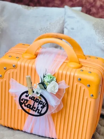 This shows how I present my kids' activity hampers. This bright orange suitcase is decorated with a "Happy Rakhi" tag and elegant ribbons, creating an exciting gift that children will love to open.