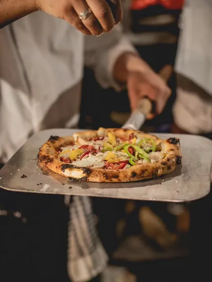 A chef adds the finishing sprinkle of cheese onto a perfectly baked wood-fired pizza. This close-up highlights the final, personal touch that makes each dish special at our live pizza station.