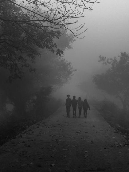 A group of friends walks down a path into the dense fog. This black and white image evokes a sense of mystery, journey, and togetherness.
