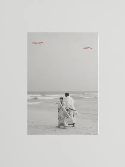 A black and white photo of a couple on the beach, framed with the words 'amoolya anand' (precious joy). This artistic composition turns a simple moment into a poetic statement.