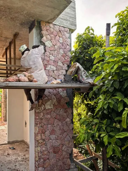 A local mason carefully applies coral stone to a structural column at Kizikula. This cladding technique requires great skill and gives the modern concrete structure a traditional, handcrafted finish.