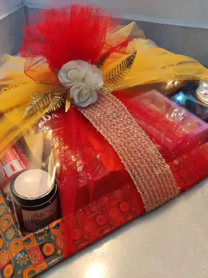 A beautifully wrapped wedding hamper in red and yellow net, filled with a mix of sweet and savory items.
