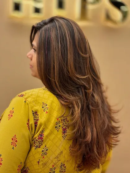 A side view of long, layered hair with fresh highlights. The color enhances the texture and movement of the cut.