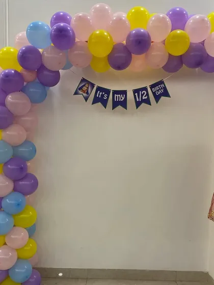 A cute and simple decoration for a half-birthday celebration, featuring a pastel-colored balloon arch and an "It's my 1/2 Birthday" banner.