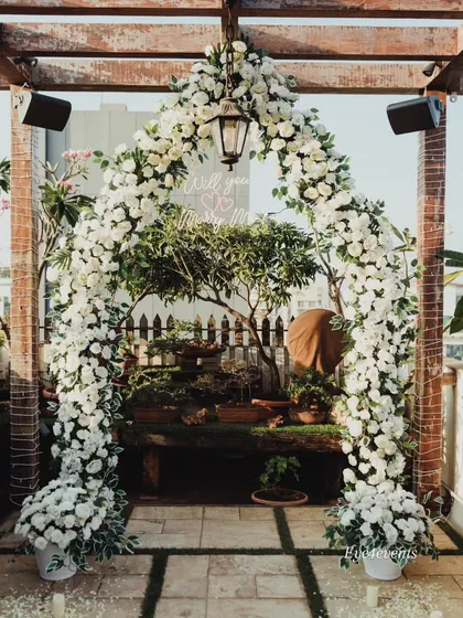 A lush and rustic floral arch made entirely of white flowers frames this beautiful rooftop proposal space. The natural wood of the pergola combined with the elegant white decor creates a stunning contrast.
