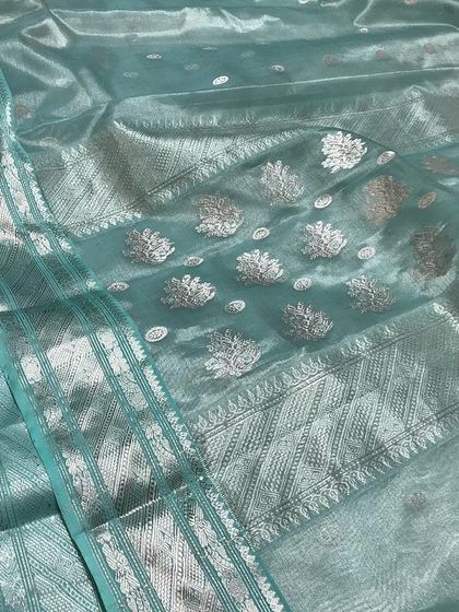 A shimmering light blue organza or tissue sari with intricate silver zari work, a perfect example of modern elegance.