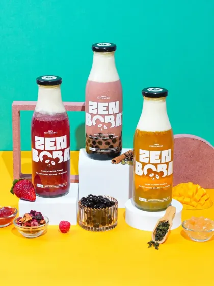 A clean and modern product shot for Zen Boba, showcasing three different flavors in their branded bottles. This style uses bold, colorful backdrops and minimal props to make the packaged product the hero, perfect for e-commerce and advertising.