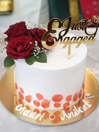 A close-up of a custom engagement cake for Gauri and Aniket. The design features a modern painted effect at the base, topped with fresh roses and a "Just Engaged" topper.