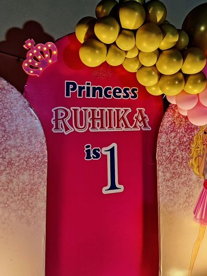 A close-up of a princess-themed first birthday backdrop, featuring Barbie and a crown detail.
