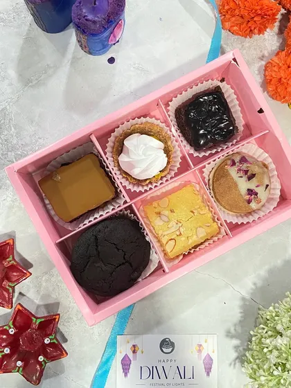 My "Joyfull Diwali Pack" featuring six different treats. This box includes a brownie, a baked Lotus Biscoff cheesecake bite, a lemon tart, and a Rasmalai cookie sandwich.