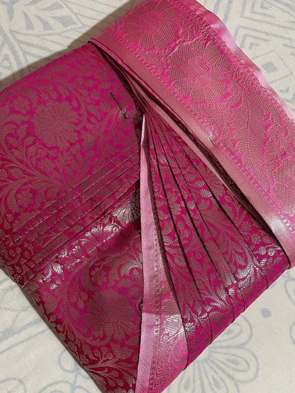 A striking magenta silk saree with silver zari work. The pleats are crisp and ready to create a stunning silhouette.