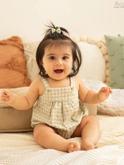 This baby girl's bright smile and gingham romper are the definition of cute. Her happy energy is contagious.