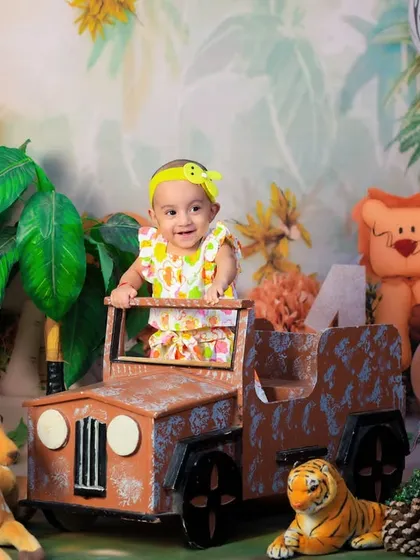A one-year-old girl in a cute yellow outfit, standing in our jungle jeep setup. Her happy expression says it all.
