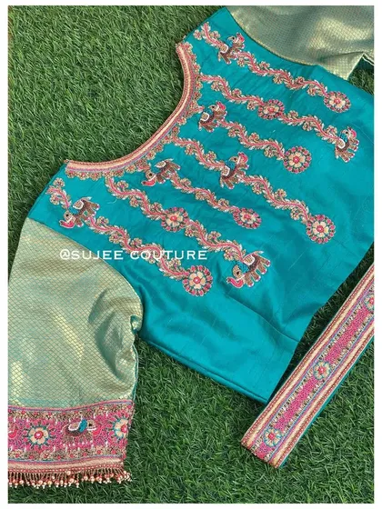 A teal blouse featuring vertical rows of peacock and floral embroidery. The contrasting brocade sleeves have an embroidered border that ties the color palette together.
