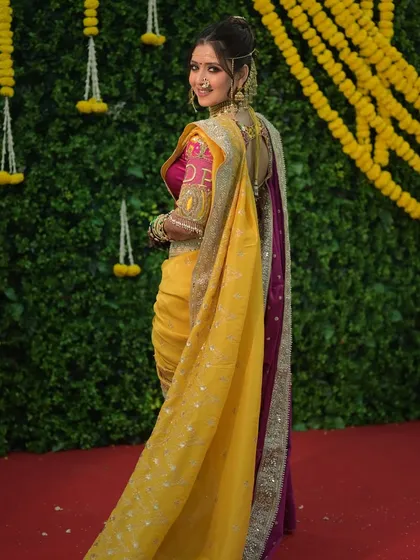 A full view of this bride's Maharashtrian engagement look. The vibrant yellow and purple saree is balanced with a soft, authentic makeup style that lets her natural beauty shine.