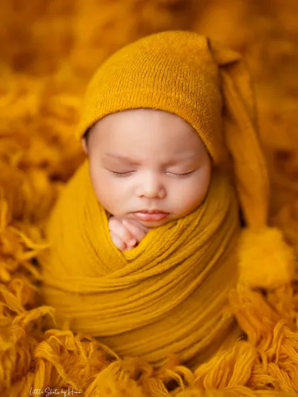 A close-up of a baby snugly wrapped in a mustard yellow swaddle and a cute pom-pom hat. The texture of the wrap adds depth and coziness.