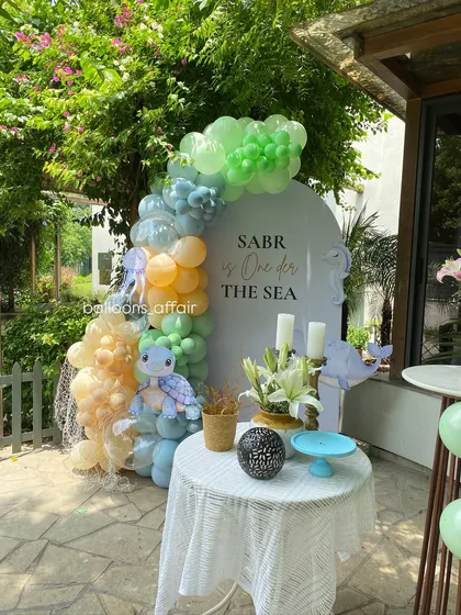 An 'Under the Sea' themed first birthday party. This outdoor setup features a custom backdrop and a balloon garland in ocean colors with a cute turtle plushie.