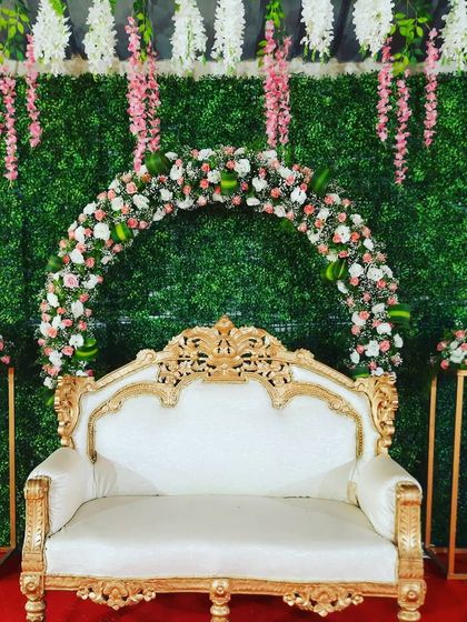 A full view of the garden-themed engagement stage. The combination of the green wall, floral arch, and classic seating creates a beautiful setting for photos.