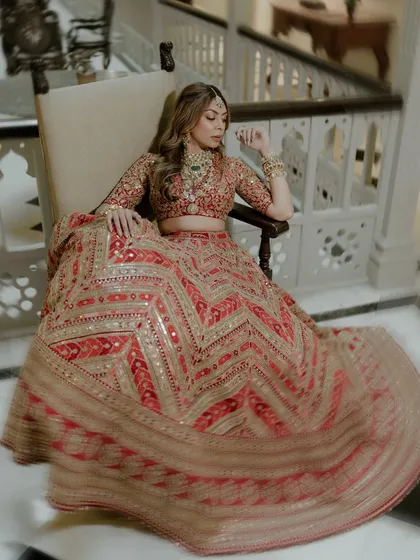 A moment of quiet contemplation. The bride, in her stunning red and gold Sabyasachi lehenga, sits gracefully, the twirl of her skirt creating beautiful lines and texture.