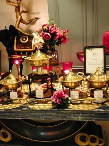We believe in presentation that speaks of luxury. This buffet display showcases our collection of ornate, polished brass chafing dishes, each holding a different delicacy, complemented by fresh floral arrangements for a royal touch.