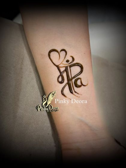A close-up of the "Maa Paa" ambigram tattoo, a simple yet powerful design that beautifully complements the main portrait for a Mundan ceremony. It's a symbol of parental love etched in henna.