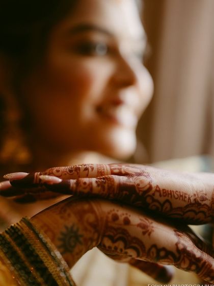 A close-up shot focusing on the bride's hands, showing her intricate henna with the groom's name subtly written in it.