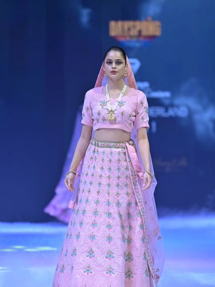 This pastel pink lehenga features delicate, repeating motifs embroidered in soft green and blue threads. It’s a subtle, elegant take on traditional bridal wear, perfect for a daytime wedding.