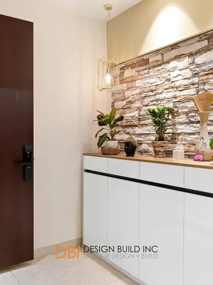 A contemporary foyer with a white storage cabinet set against a textured stone wall. The space is decorated with potted plants, creating a fresh and welcoming entrance.