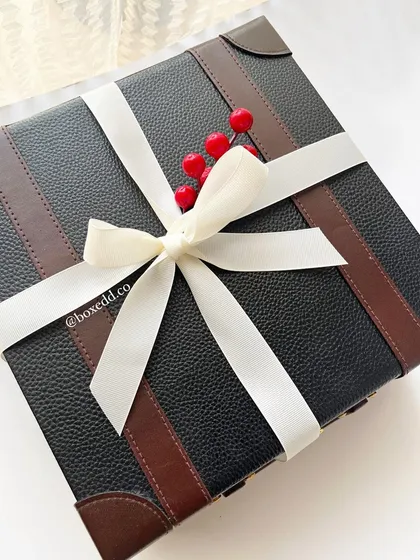 A luxury leather-finish trunk box tied with a simple white ribbon and a sprig of holly. This packaging is perfect for premium New Year and Christmas corporate gifts.