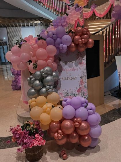 A welcome sign for a butterfly themed first birthday, adorned with a beautiful arrangement of pink, purple, and yellow balloons.