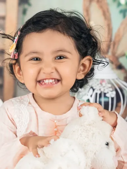 A beautiful, bright smile from this little girl holding her teddy bear. A simple, heartwarming portrait.