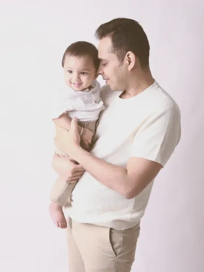 A father holds his smiling son close. The simple white background puts all the focus on their happy and loving connection.