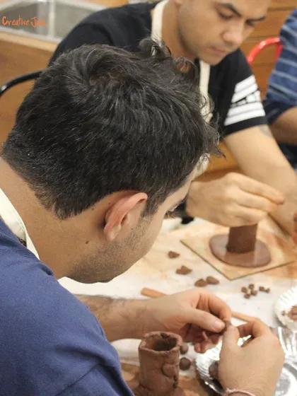Two men are focused on their clay projects, carefully shaping and adding details to their hand-built pottery pieces.