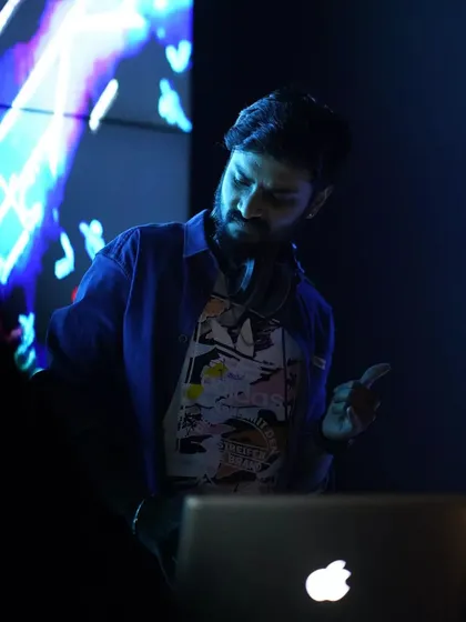 In the zone, mixing tracks with my headphones on. The background shows a glimpse of the complex blue visuals I use to complement the music, embodying my "MIND & GRIND" philosophy.