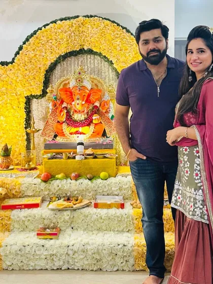 A happy client couple standing before their beautiful yellow floral Ganpati mandap. The traditional color scheme is perfect for creating a warm and festive atmosphere at home.