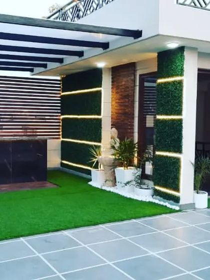 A luxurious terrace design featuring a bar under a pergola, a vertical garden, and a stunning backlit Buddha wall art piece. The grey tiled floor adds a modern touch.