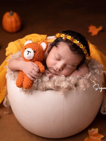 A newborn girl in a pumpkin-themed setup, perfect for an autumn baby. The warm orange and yellow tones create a cozy feel.