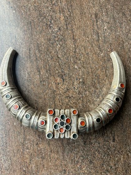 A tribal-style oxidised silver necklace. This rigid, crescent-shaped piece is adorned with colourful stone inlays.