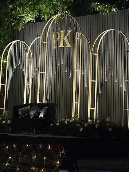 A modern Sangeet stage with a corrugated metal backdrop and minimalist gold arches featuring the couple's monogram.