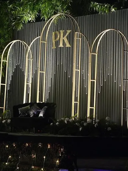 A modern Sangeet stage with a corrugated metal backdrop and minimalist gold arches featuring the couple's monogram.