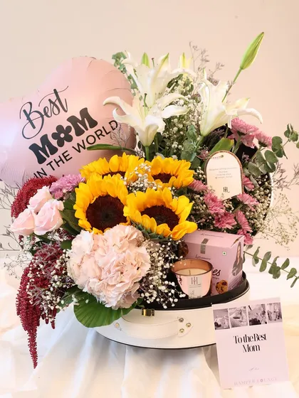 A full view of the sunflower and lily bouquet hamper. It's a cheerful and bright gift, complete with a "Best Mom in the World" balloon and a personalized card.