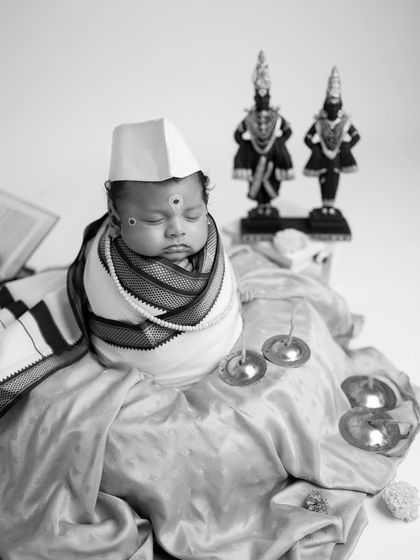 A black and white portrait of the baby as a little Warkari, with traditional cymbals placed nearby. The focus is on the baby's peaceful, sleeping face.