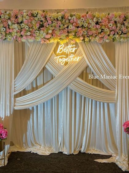 A sophisticated backdrop with intricately draped cream fabric, a floral runner on top, and a 'Better Together' neon sign. This design is perfect for creating an elegant and luxurious feel.